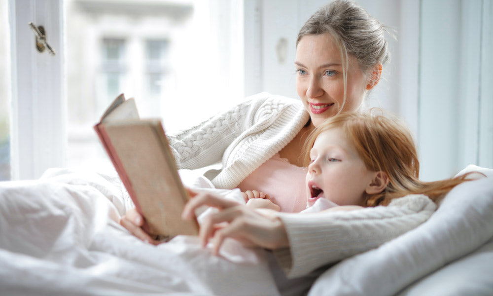 mom and daughter reading a book in bed