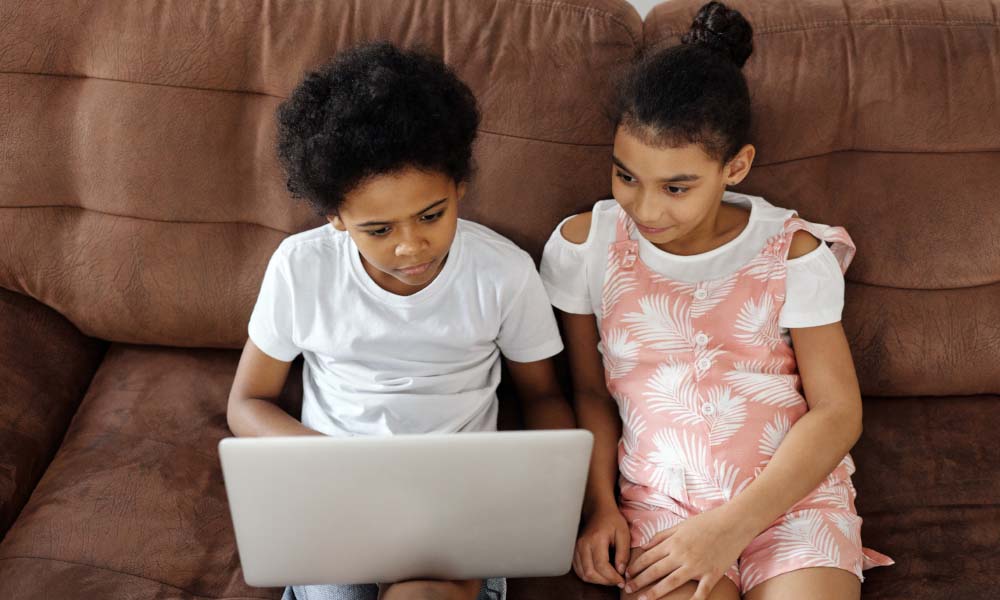 siblings sitting on a couch and looking at a computer