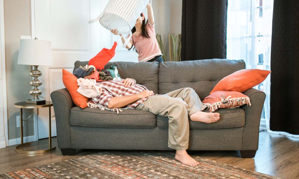 woman throwing laundry on man laying on couch