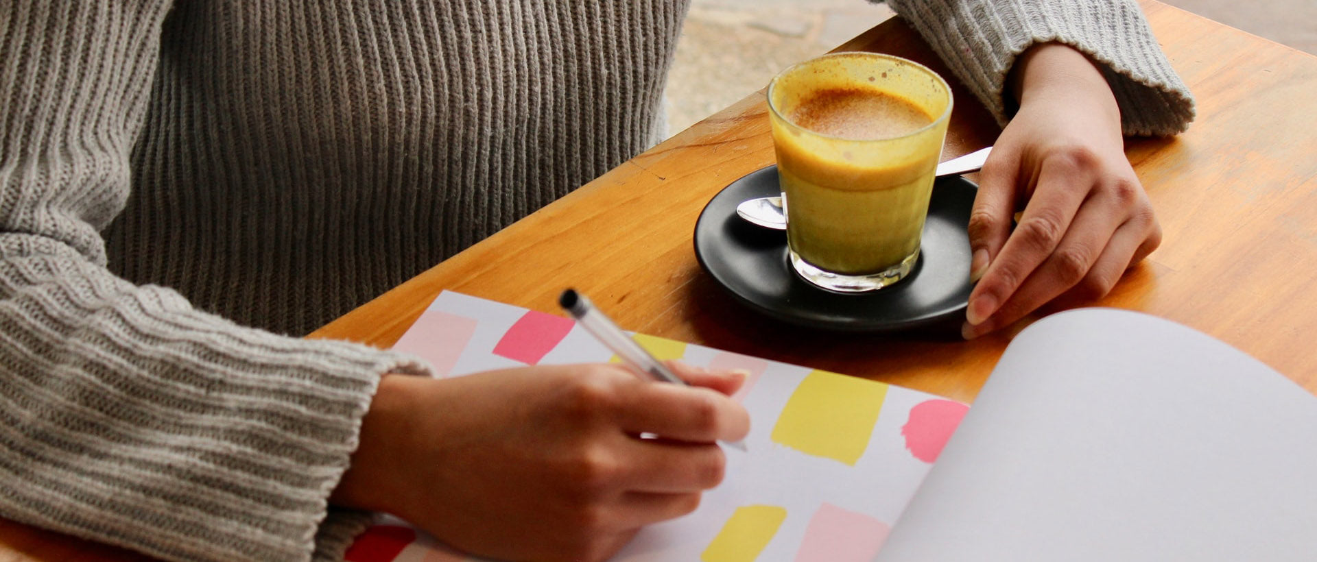 person holding pen with coffee on table