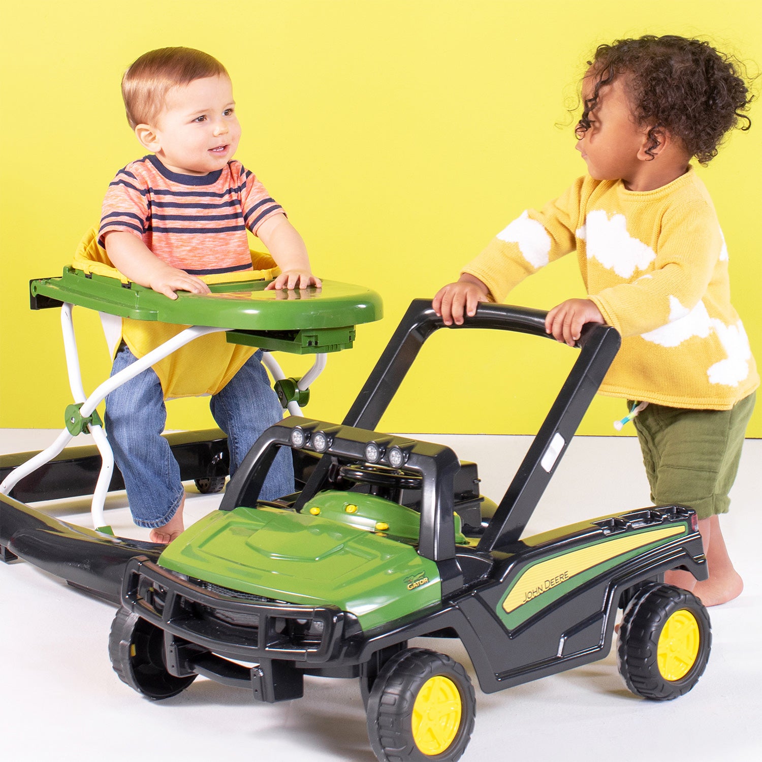 Two children playing with a toy lawn mower against a yellow background
